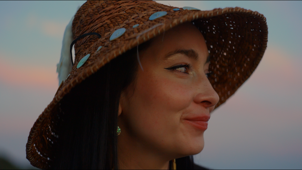 Janna Wale, wearing a cedar hat, looks to the side, smiling slightly.