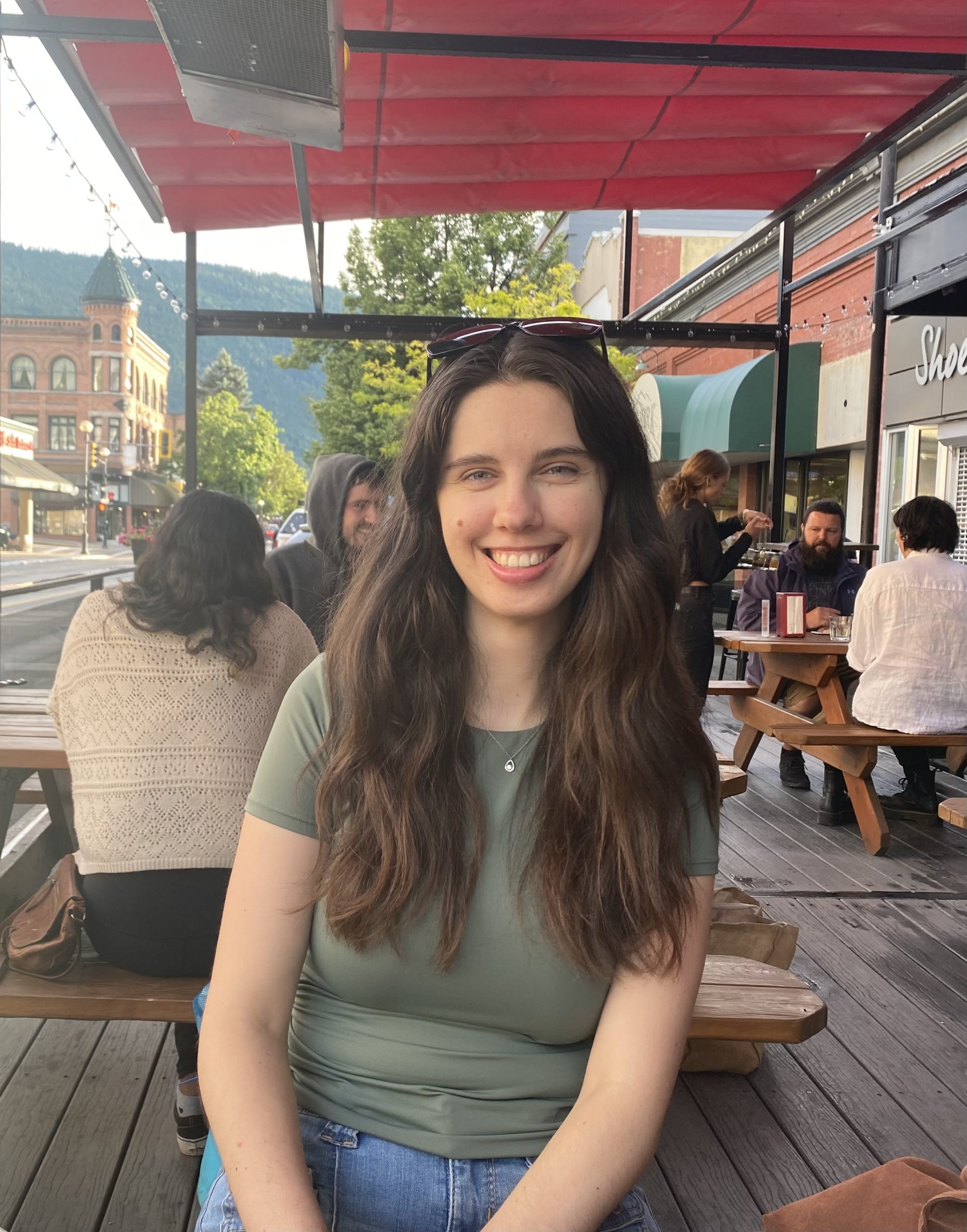 PICS climate intern Andra Tarta sitting at a table in Nelson, B.C., smiling at the camera. 
