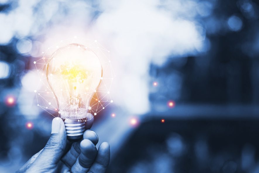 A hand holds a glowing lightbulb emitting sparks