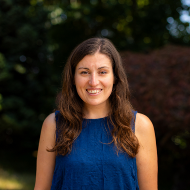 Emma Claydon smiles and looks at the camera, She is wearing a blue sleeveless shirt.